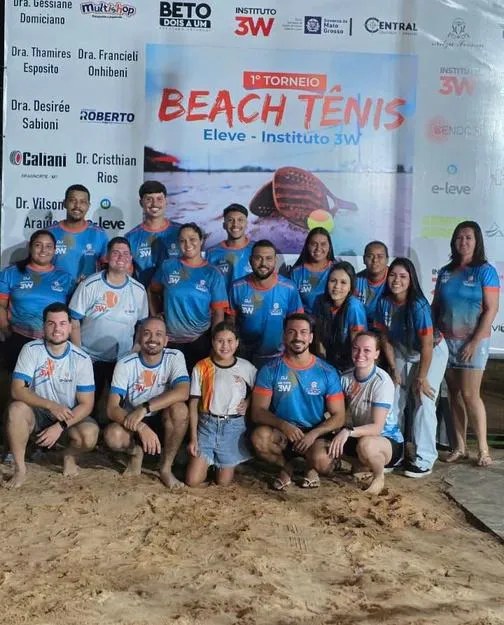 Atletas na areia em frente ao painel do 1º Torneio de Beach Tennis.