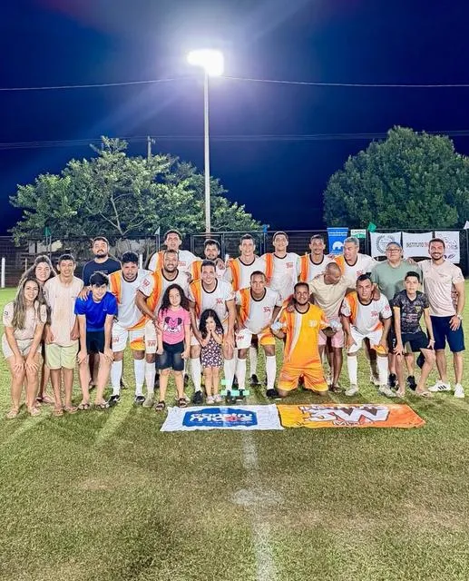 Time de futebol adulto e familiares em campo à noite.