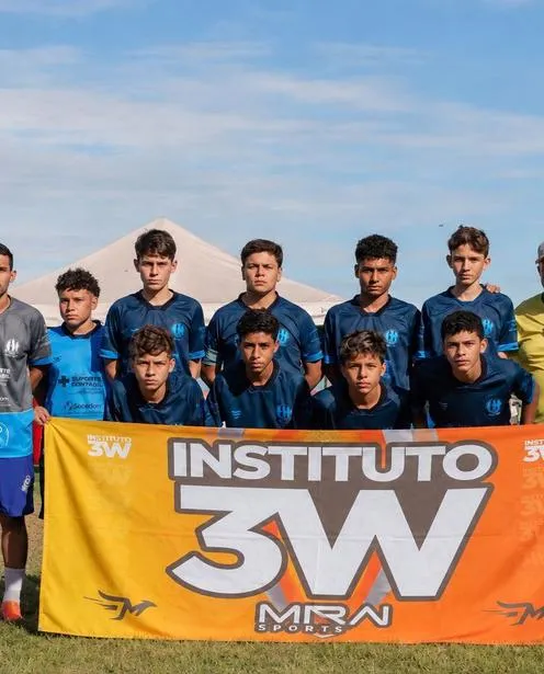 Time de futebol de base posando com a bandeira laranja do Instituto 3W.