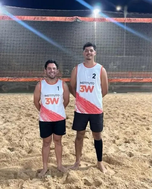 Dupla de vôlei de praia com camisetas do Instituto 3W na quadra de areia.